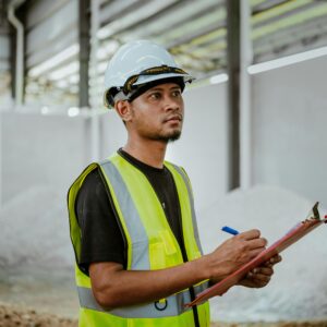Asian construction worker in a factory setting, using a clipboard for inspection tasks in Banting, Malaysia.