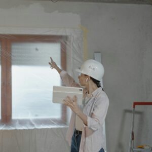 Woman in hard hat using tablet to oversee home renovation in a partially completed room.